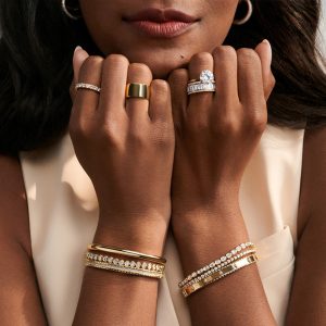 kadın bileğinde diğer bilekliklerle birlikte kullanılan oval kesim bezel suyolu pırlanta bileklik